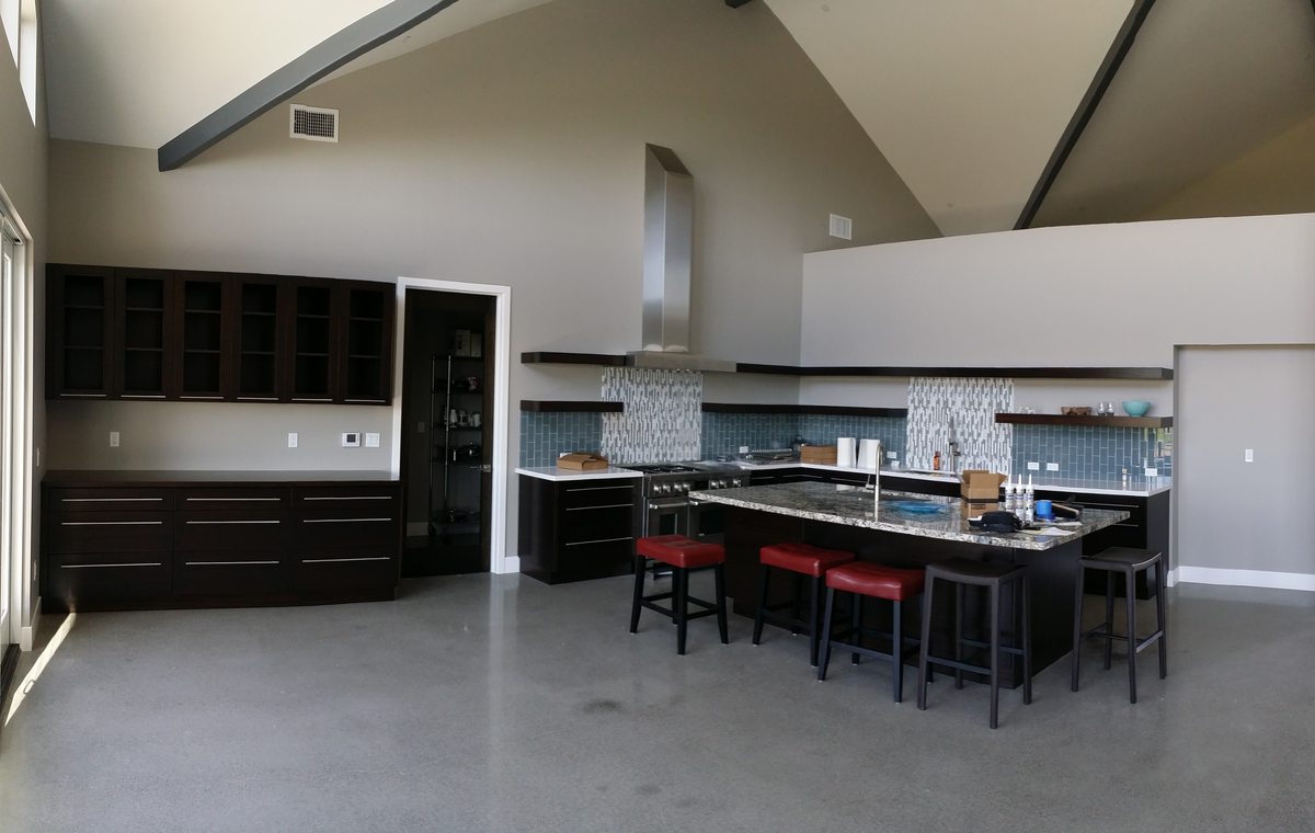 A large open kitchen with black cabinetry, open shelves and an island with red stools under a vaulted ceiling.