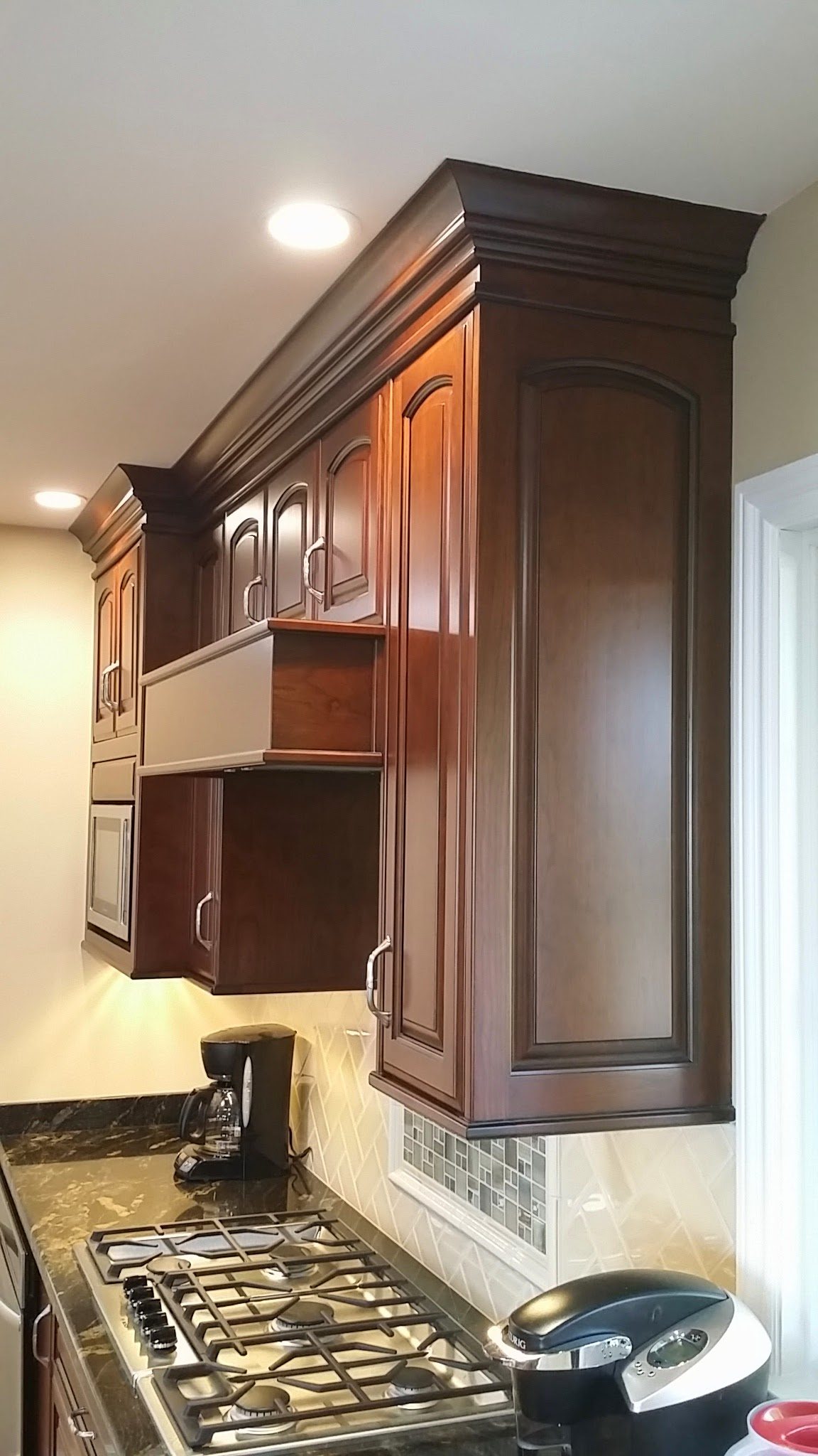 Tall cherry cabinets with crown molding over a range, with under-cabinet lights.