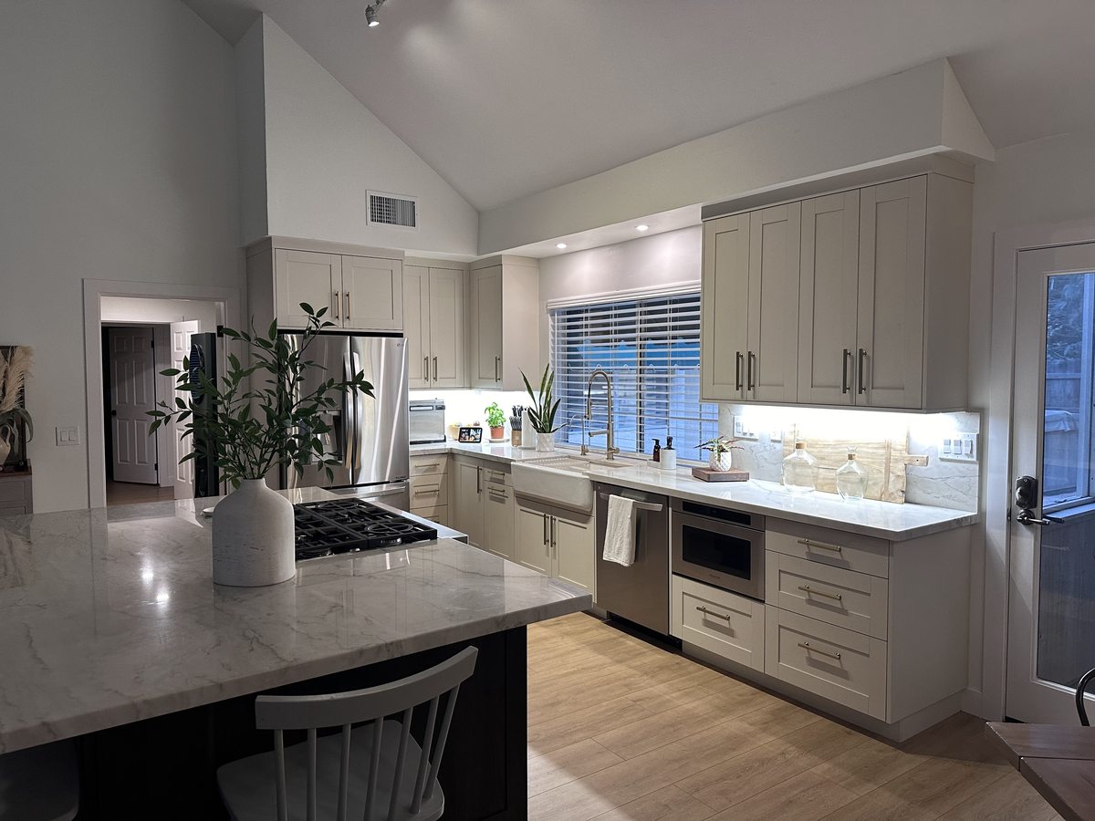 A bright kitchen with pale gray shaker cabinets, a white stone island and under-cabinet lighting.