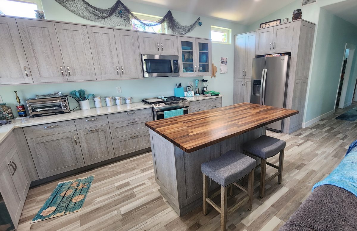 A kitchen with gray-washed cabinets and an island topped in butcher block, with two stools.