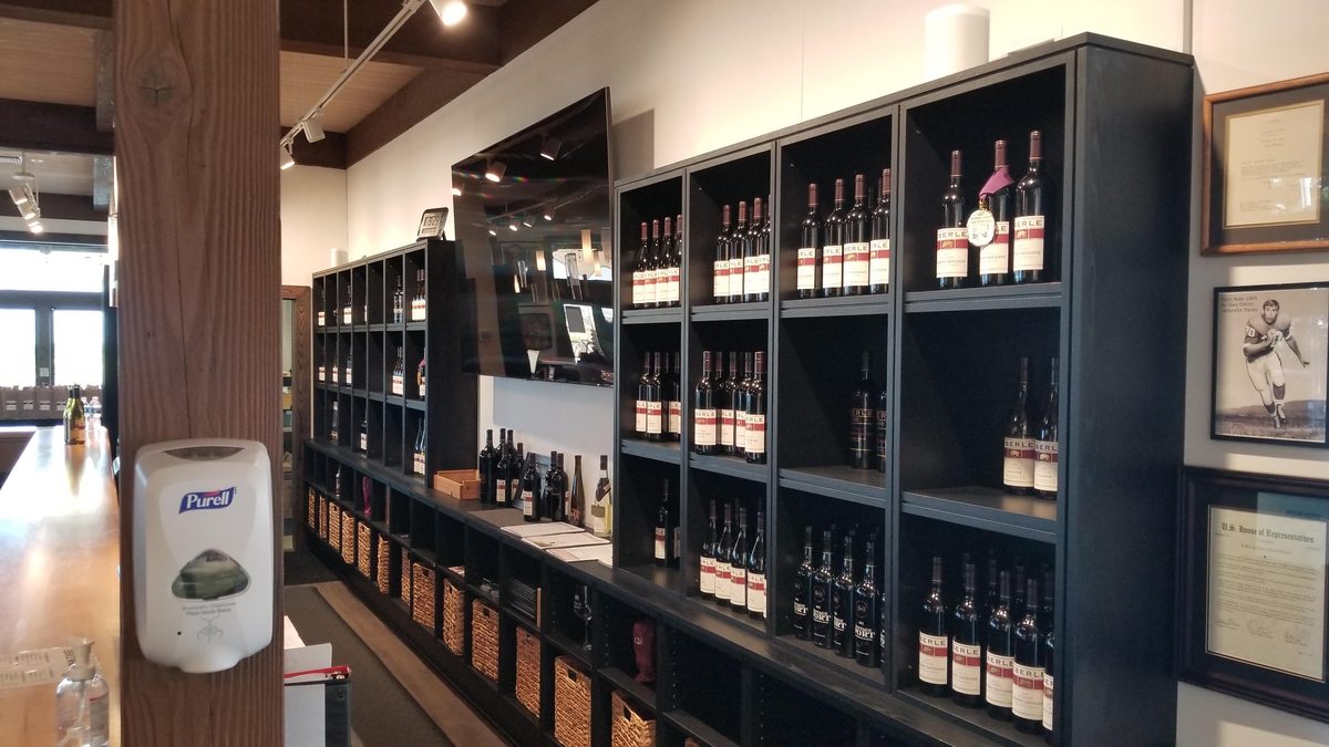 Dark wood wine shelving lining a wall in a shop, stocked with bottles.